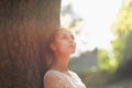 Thoughtful young woman lean against tree