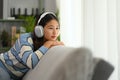 Thoughtful young woman listening to calm music in headphone and looking away while relaxing on couch Royalty Free Stock Photo