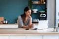 Thoughtful young woman looking her laptop while holding a cup of coffee in the kitchen at home Royalty Free Stock Photo