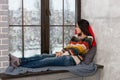 Thoughtful young woman lying down on the pillows on the windowsill and looking out the window while snowing Royalty Free Stock Photo