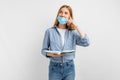 Thoughtful young woman in a medical mask on her face, with books on a white background