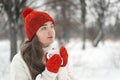 Thoughtful young woman in winter park with cup in hands drink something. Girl in red knitted hat and mittens on winter outside