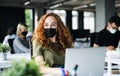Young woman with face mask back at work in office after lockdown.