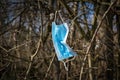 Thoughtlessly discarded protective mask against SARS-Covid-19 hanging in a bush