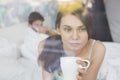 Thougtful woman having coffee at home with man lying in background