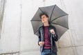 Thougtful young teen man standing in rain in city with umbrella