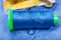 Thread bobbin, button, measure tape on blue cloth