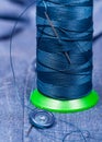 Thread bobbin with needle, button on blue cloth