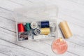 thread needles sewing supplies in a plastic box on a wooden background