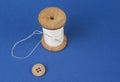 Thread on wooden reel with needle and button on blue. Royalty Free Stock Photo