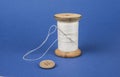 Thread on wooden reel with needle and button on blue. Royalty Free Stock Photo