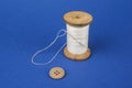 Thread on wooden reel with needle and button on blue. Royalty Free Stock Photo