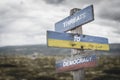 threaths to democracy text quote on wooden signpost outdoors on nato colored flag, ukrainian flag and russian flags