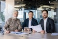 Three adult businessmen in suits sitting at the table in the office, having a work meeting, smiling and looking at the Royalty Free Stock Photo