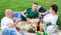 Three adult men enjoying picnic outdoors on summer day