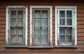 Three aged windows shown on wooden plank facade. White frames peeling off paint. Old home architecture with worn construction. Royalty Free Stock Photo