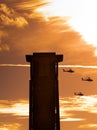 Three apache helicopters flying past a tower with clouds