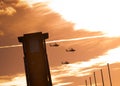 Three apache helicopters flying past a tower with clouds