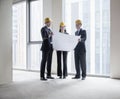 Three architects in hardhats examining a blueprint in an office building