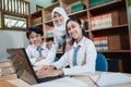 three Asian high school students smile into the camera while studying together using a laptop Royalty Free Stock Photo