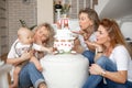 Three attractive middle-aged and young women blowing kisses to little one-year-old boy touching bear on birthday cake. Royalty Free Stock Photo