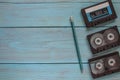 Three audio cassettes and a simple pencil lie on a blue wooden background. Space for the text