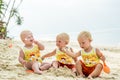 Three baby Toddler sitting on a tropical beach in Thailand and playing with sand toys. The yellow shirts. Two boys and one girl Royalty Free Stock Photo