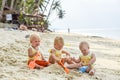 Three baby Toddler sitting on a tropical beach in Thailand and playing with sand toys. The yellow shirts. Two boys and one girl Royalty Free Stock Photo