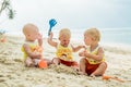 Three baby Toddler sitting on a tropical beach in Thailand and playing with sand toys. The yellow shirts. Two boys and one girl Royalty Free Stock Photo