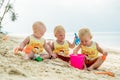 Three baby Toddler sitting on a tropical beach in Thailand and playing with sand toys. The yellow shirts. Two boys and one girl Royalty Free Stock Photo