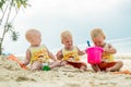 Three baby Toddler sitting on a tropical beach in Thailand and playing with sand toys. The yellow shirts. Two boys and one girl Royalty Free Stock Photo