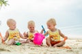 Three baby Toddler sitting on a tropical beach in Thailand and playing with sand toys. The yellow shirts. Two boys and one girl Royalty Free Stock Photo