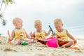 Three baby Toddler sitting on a tropical beach in Thailand and playing with sand toys. The yellow shirts. Two boys and one girl Royalty Free Stock Photo