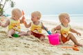 Three baby Toddler sitting on a tropical beach in Thailand and playing with sand toys. The yellow shirts. Two boys and one girl Royalty Free Stock Photo