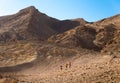 Three backpackers walking ascending mountain stone desert trail. Royalty Free Stock Photo