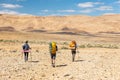 Three backpackers walking stone desert trail. Royalty Free Stock Photo