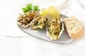 Three baked oysters Rockefeller with spinach and cheese on a small plate with lemon, bread and parsley garnish, festive appetizer