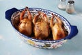 Three baked quails with lemon, orange and rosemary in a baking dish on a light blue background. Close-up