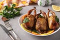 Three baked quails served with lemon, orange and parsley on a white plate on a gray background. Closeup Royalty Free Stock Photo