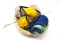 Three ball of woolen threads, yellow, blue, beige and steel knitting needles and glasses in a wooden basket on a white background.