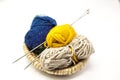 Three ball of woolen threads, yellow, blue, beige and steel knitting needles in a wooden basket on a white background. Royalty Free Stock Photo