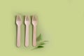 Three bamboo wood forks with a plant lie on a green background. Eco-friendly concept. Top view. Copy space