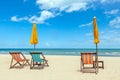 Three beach chairs with sun umbrella on beautiful beach with cloudy blue sky.