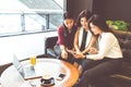 Three beautiful Asian girls using smartphone and laptop, chatting on sofa at cafe