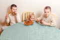 Three beautiful children sit at table in the kitchen and eat large round pancakes. Carnival Festival Royalty Free Stock Photo