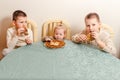 Three beautiful children sit at table in the kitchen and eat large round pancakes. Carnival Festival Royalty Free Stock Photo