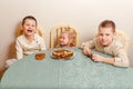 three beautiful children sit at table in the kitchen and eat large round pancakes. Carnival Festival Royalty Free Stock Photo