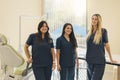 Three beautiful female dentists smile and look at camera in dental clinic