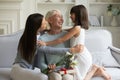 Grownup daughter granddaughter embracing elderly grandmother congratulating her with birthday