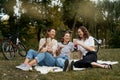 Three beautiful happy young women close friends relax in a green park on a blanket. Have fun laughing and chatting on the green Royalty Free Stock Photo